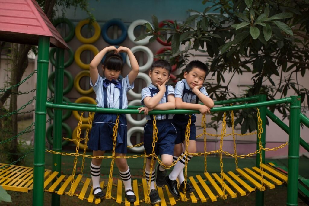 Three children in uniform having fun on a vibrant playground bridge outdoors.